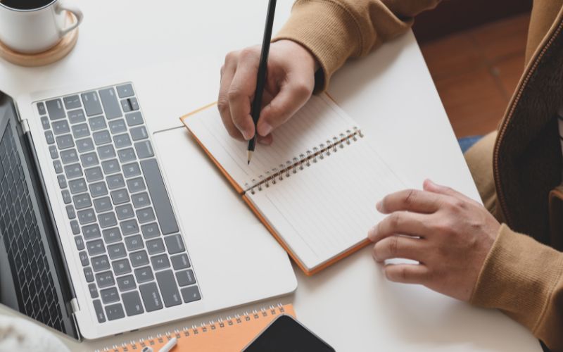 Écriture dans un carnet devant un ordinateur